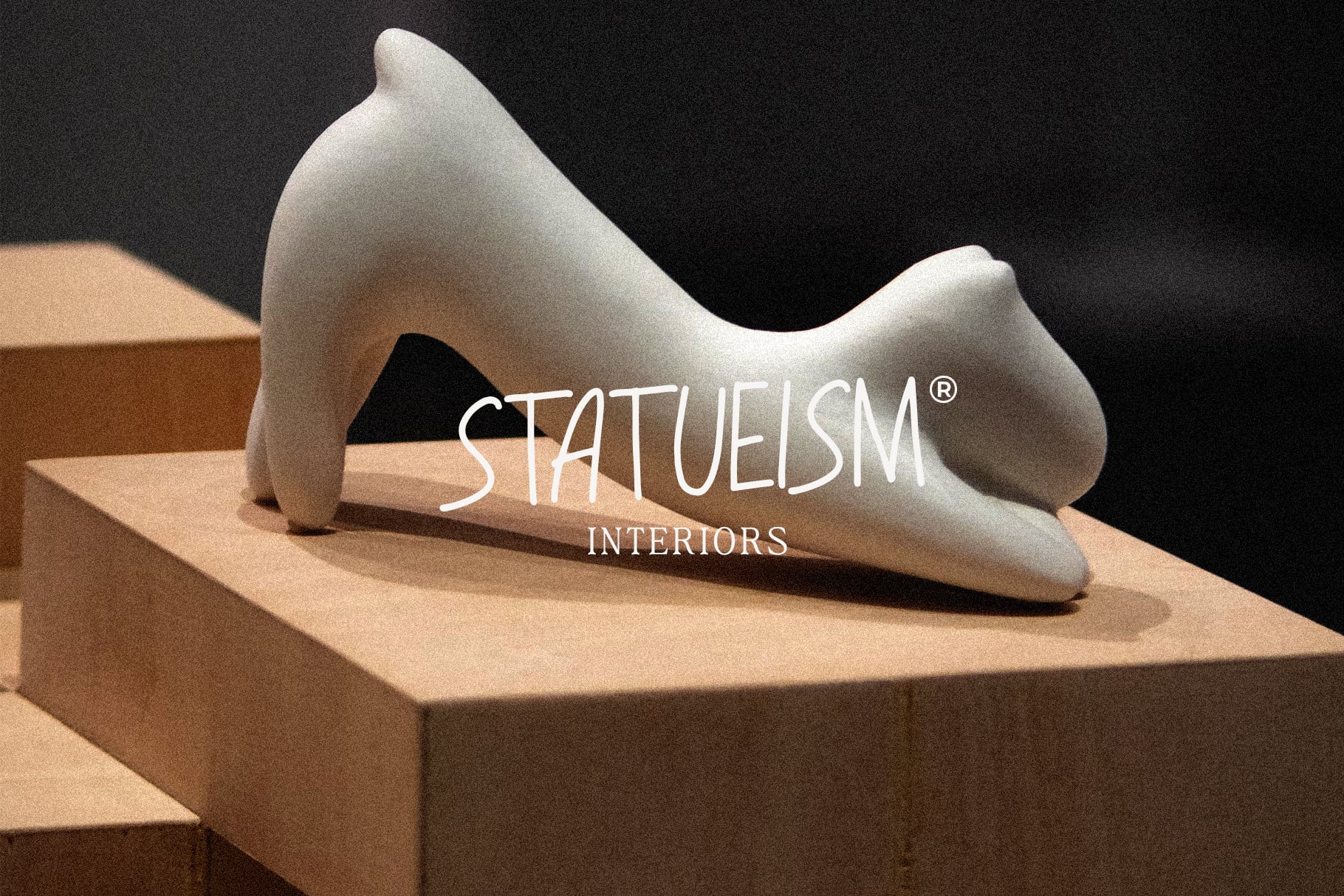White sculptural form on wooden platform with Statueism Interiors branding overlay