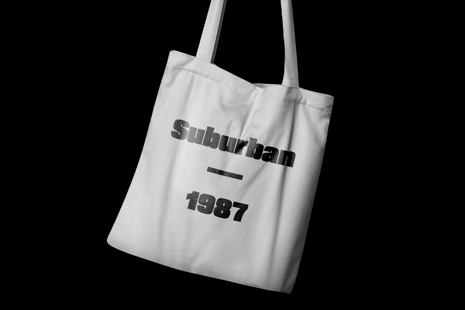 White canvas tote bag with "suburban 1987" printed in distressed typography on black background