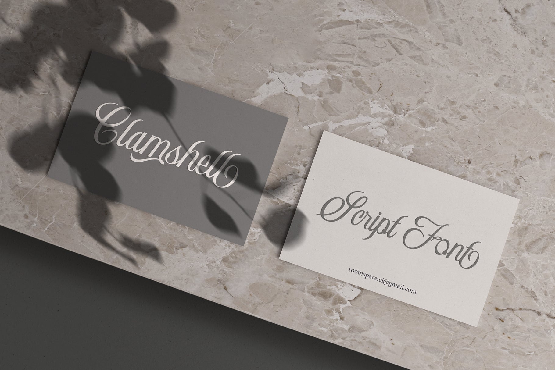 Business cards with Clamshell script font on marble surface with shadows