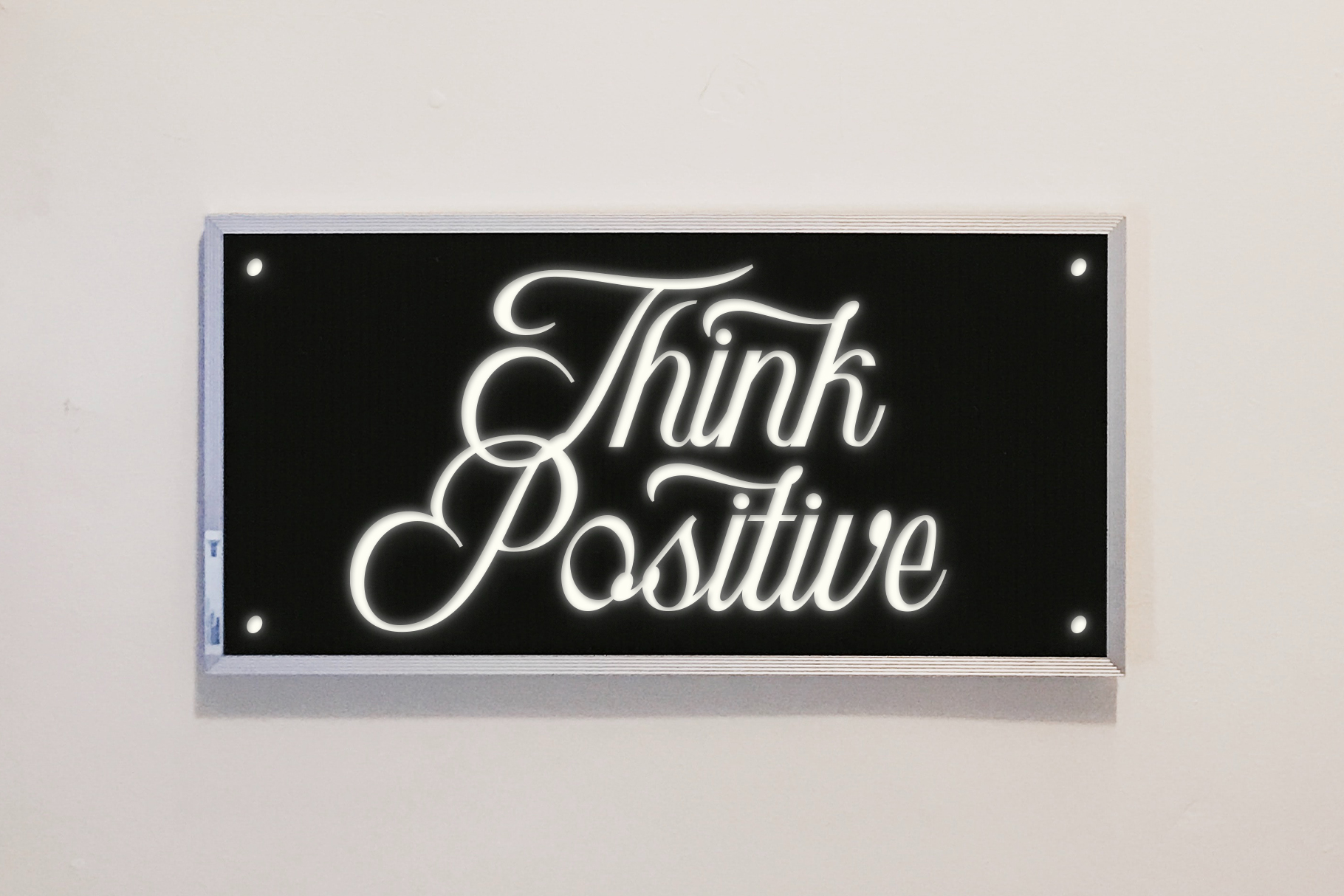 Neon sign reading Think Positive in white script on black background