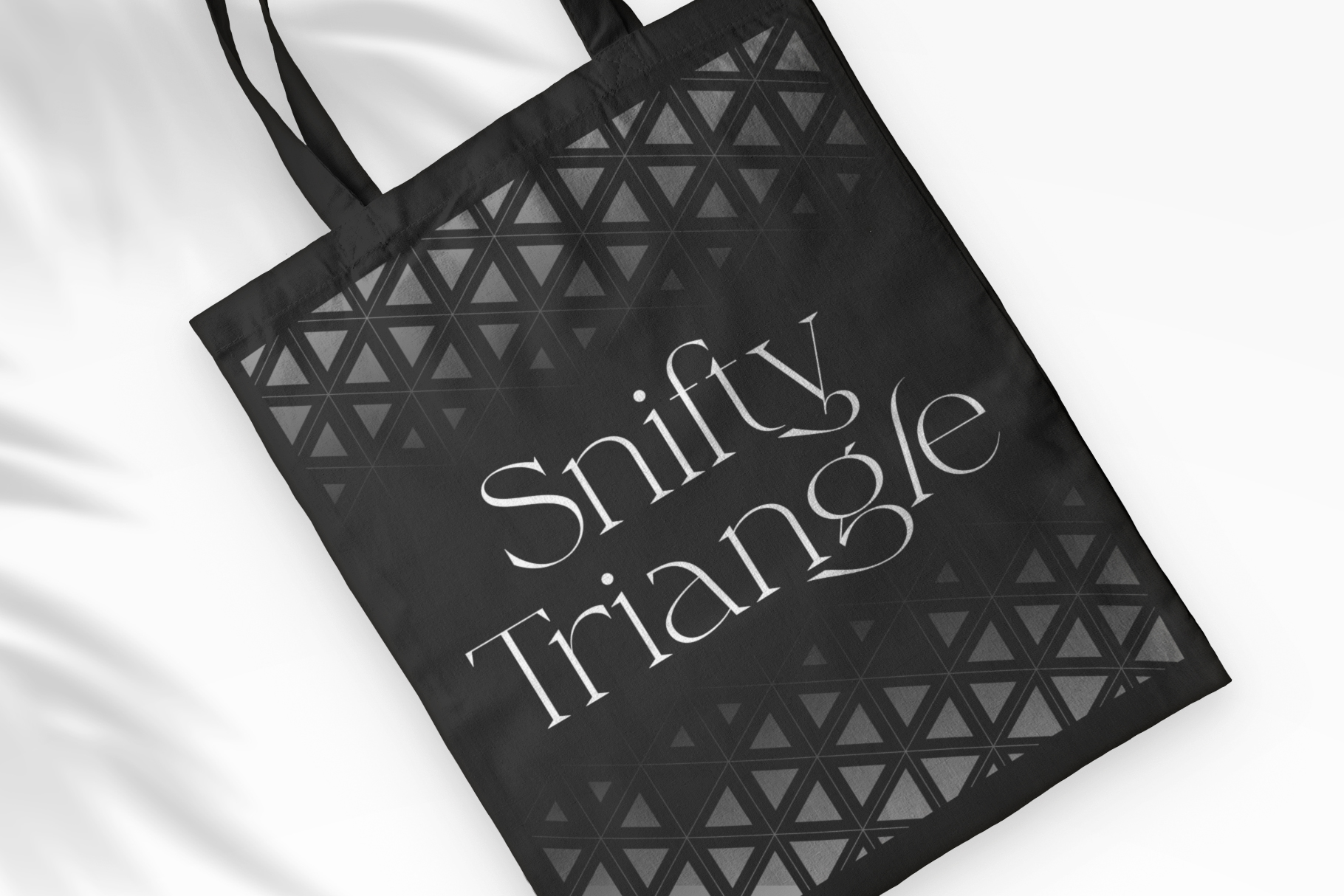Black tote bag mockup with Smifty Triangle 28 text over geometric triangle print pattern
