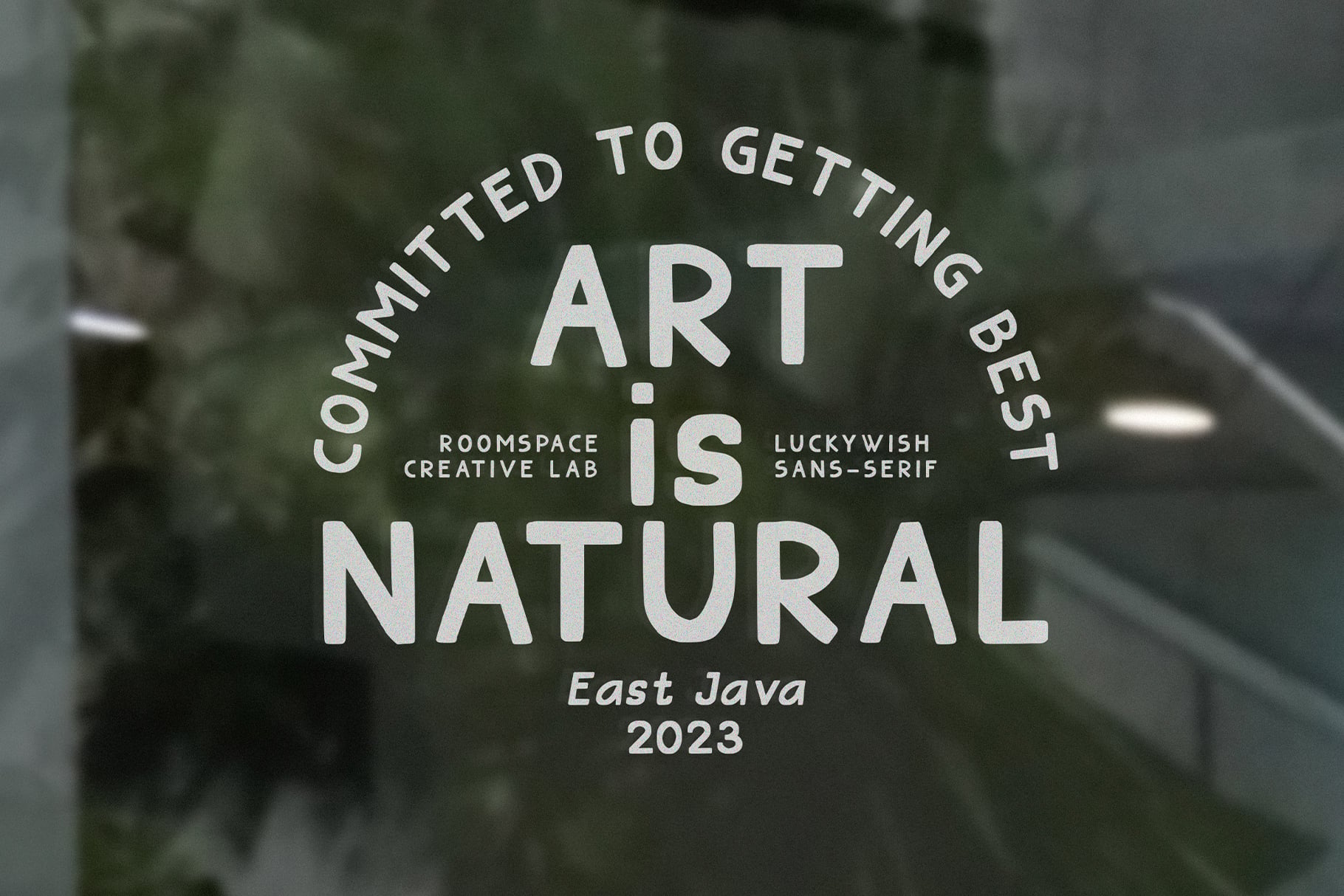 Glass window with white text reading Art is Natural, blurred greenery background visible