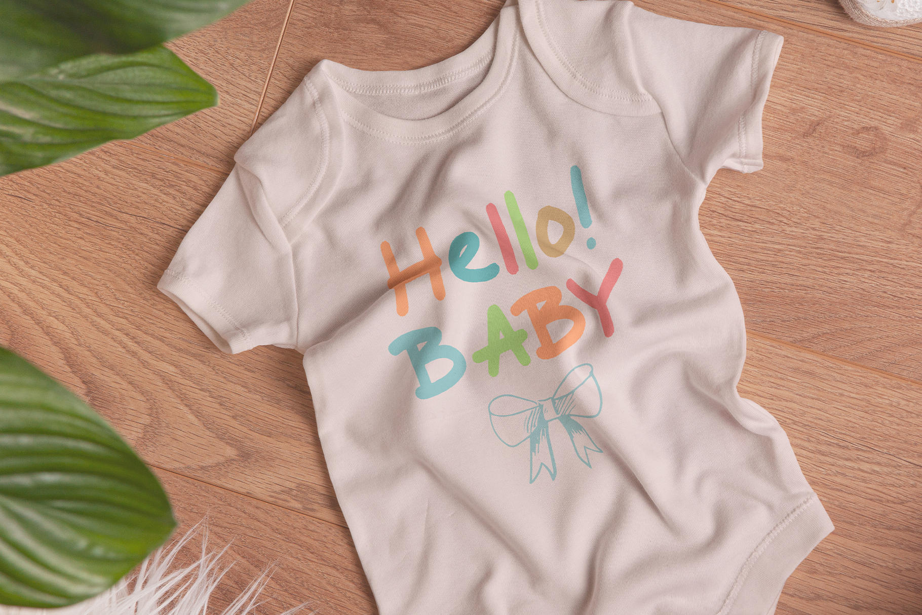 Baby onesie mockup with colorful Hello Baby text on cream fabric