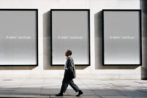Man walking past three large black-framed windows on concrete plaza