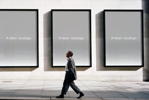 Man walking past three large black-framed windows on concrete plaza