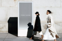 Street-level display kiosk with blank gray screen, urban setting with moving pedestrians