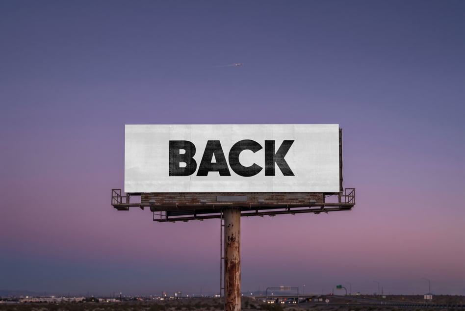 Weathered billboard with white panel saying BACK against purple sky