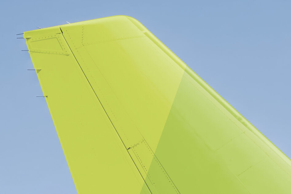 Bright yellow green aircraft tail fin against clear blue sky