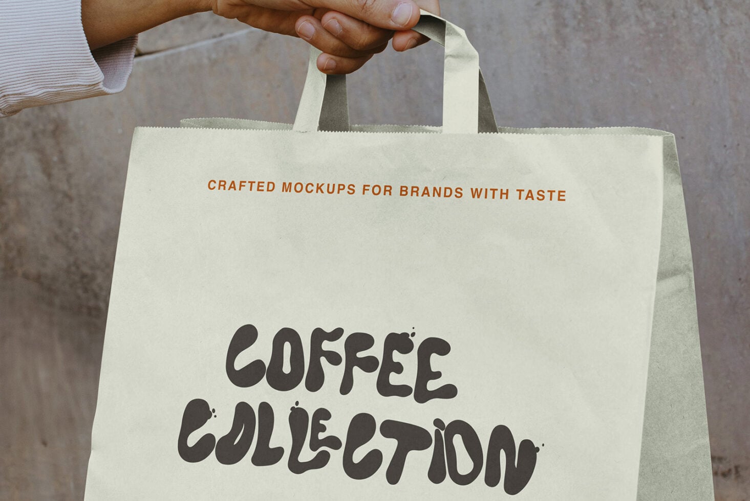Wide shot of cream paper bag with hand holding both handles showing design