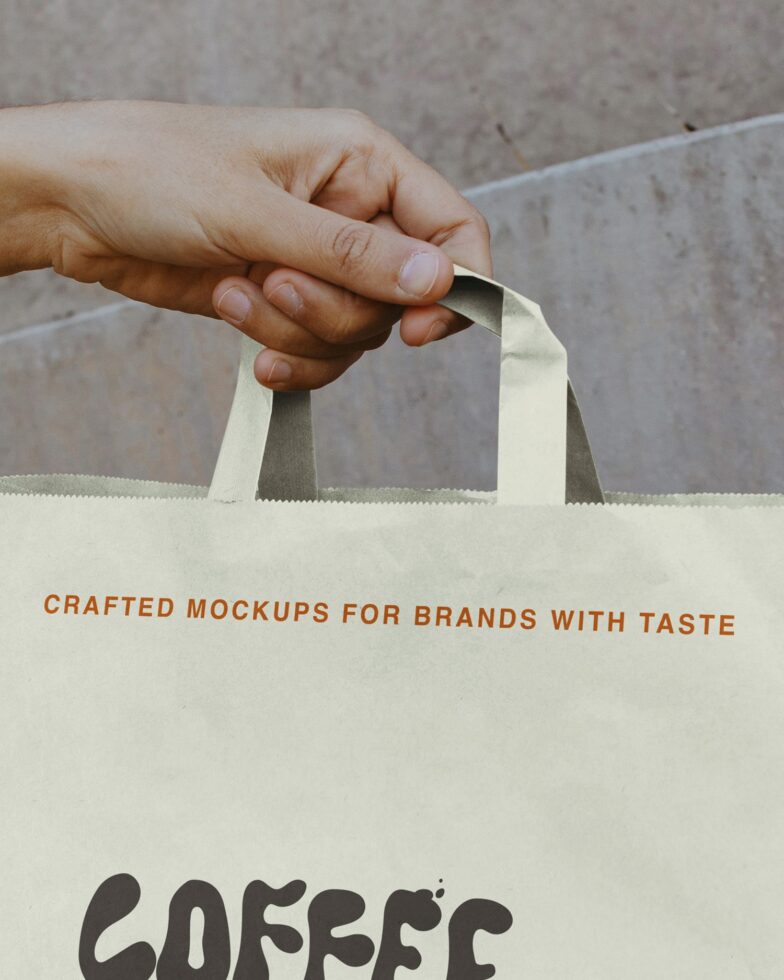 Cream paper bag with dark text held by hand showing handle detail