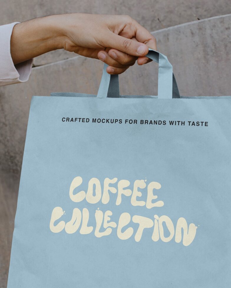 Light blue paper bag with cream lettering held by hand against concrete