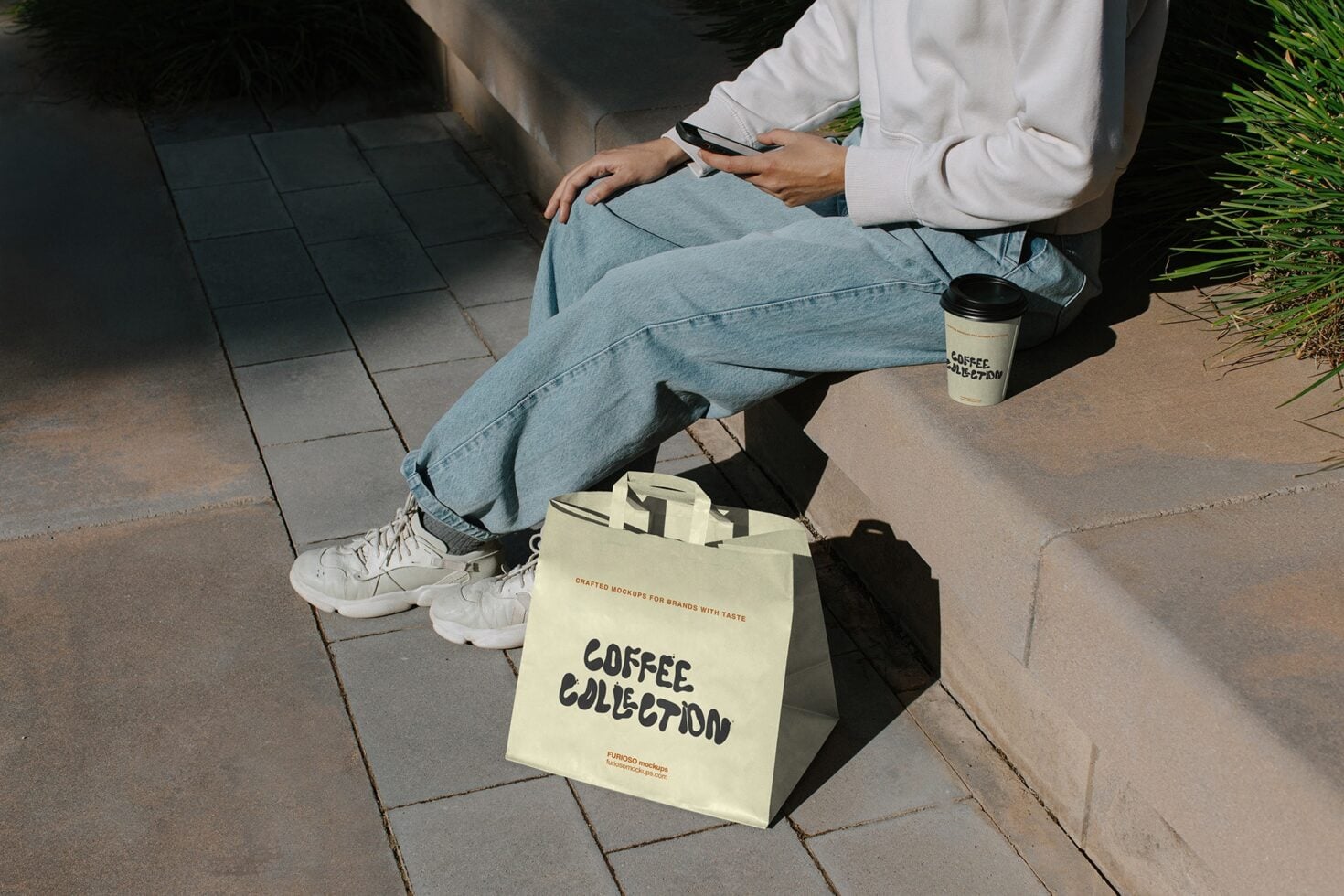 Person sitting outdoors holding phone next to cream tote bag with coffee collection branding