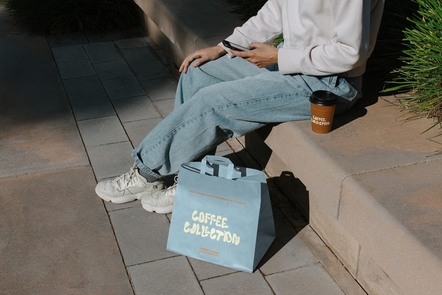 Person sitting holding coffee cup near light blue bag with Coffee Collection branding mockup