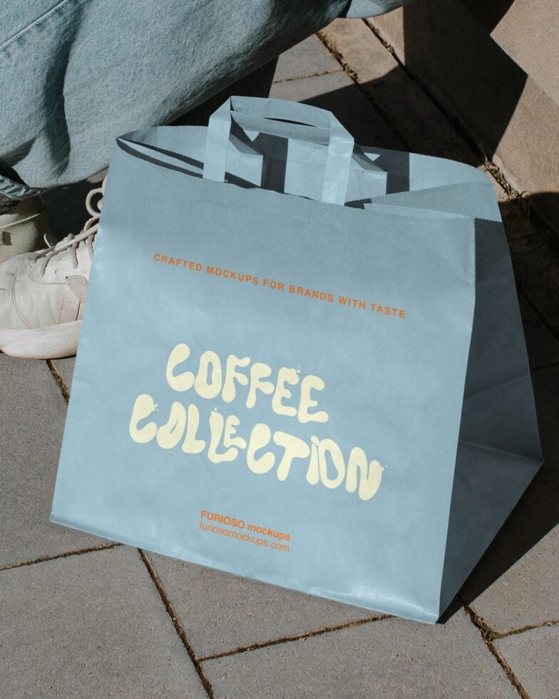 Light blue paper shopping bag with Coffee Collection text displayed outdoors on pavement