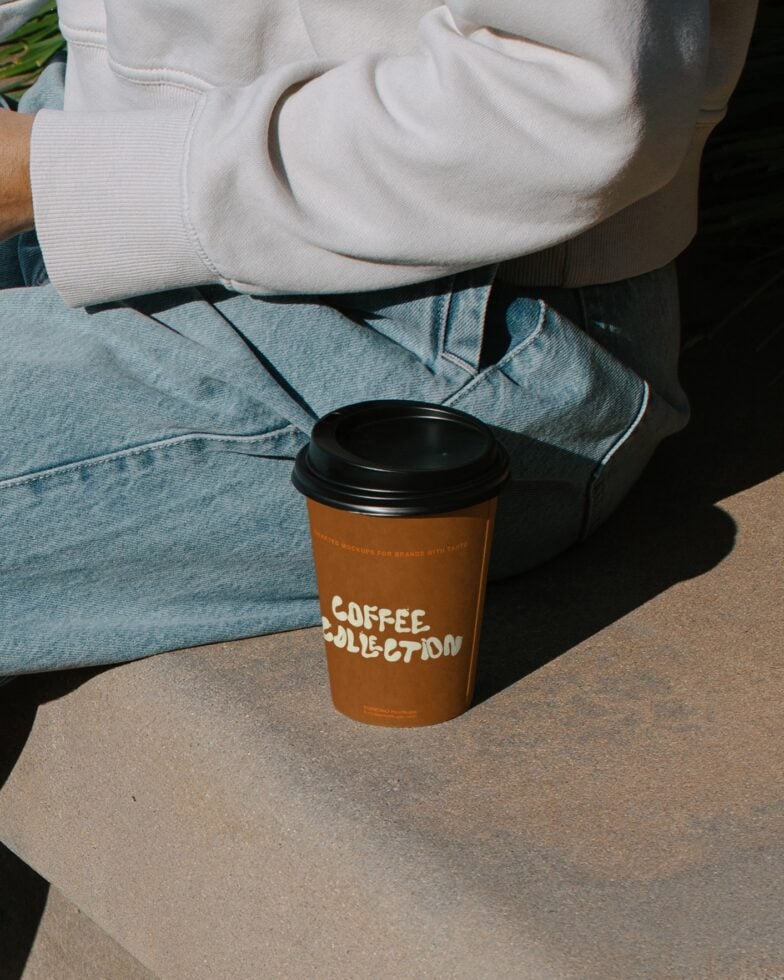 Orange takeout coffee cup with Coffee Collection branding held by person in white hoodie