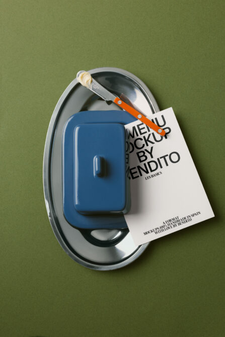 Blue kitchenware container on metal plate with orange knife, cream tag