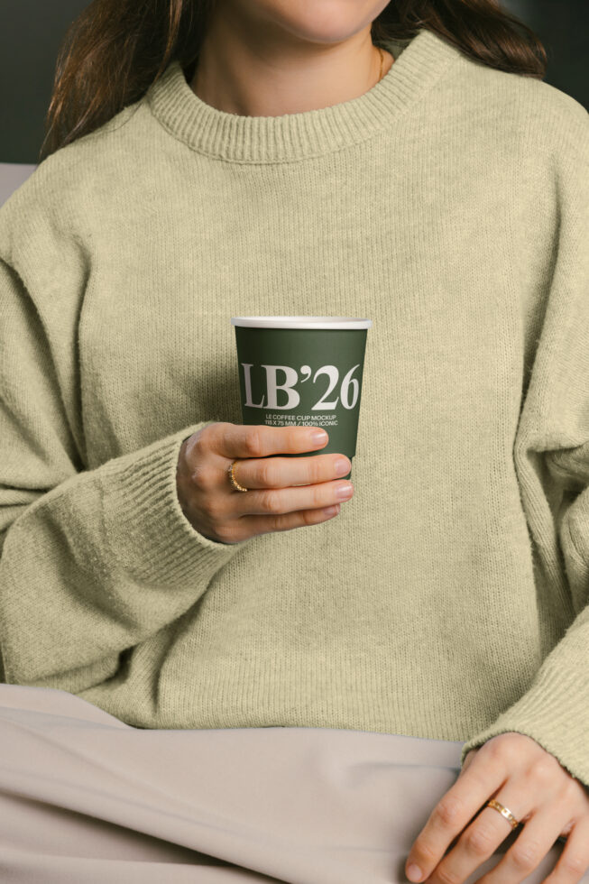 Person holding green coffee cup with LB26 label design on cream sweater