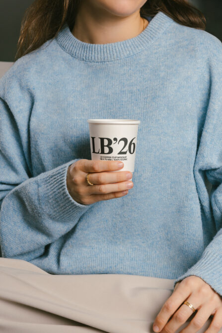 Woman in blue knit sweater holding white coffee cup with LB26 branding
