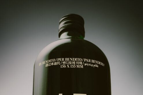 Dark green glass bottle with multilingual text printed across the back label in gold lettering