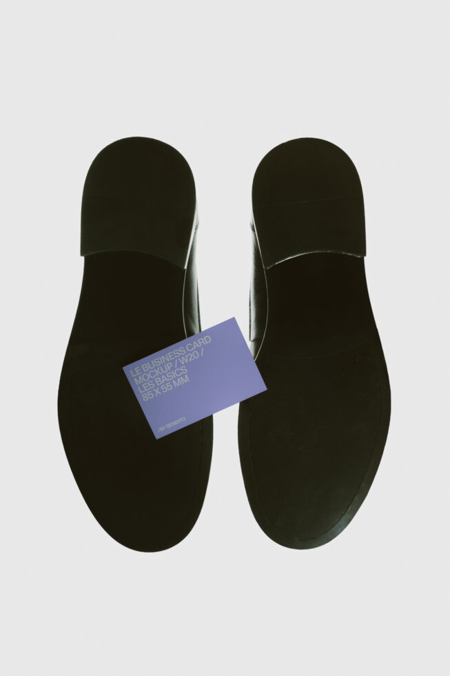 Overhead view of black slip-on shoes with periwinkle business card mockup placed between them