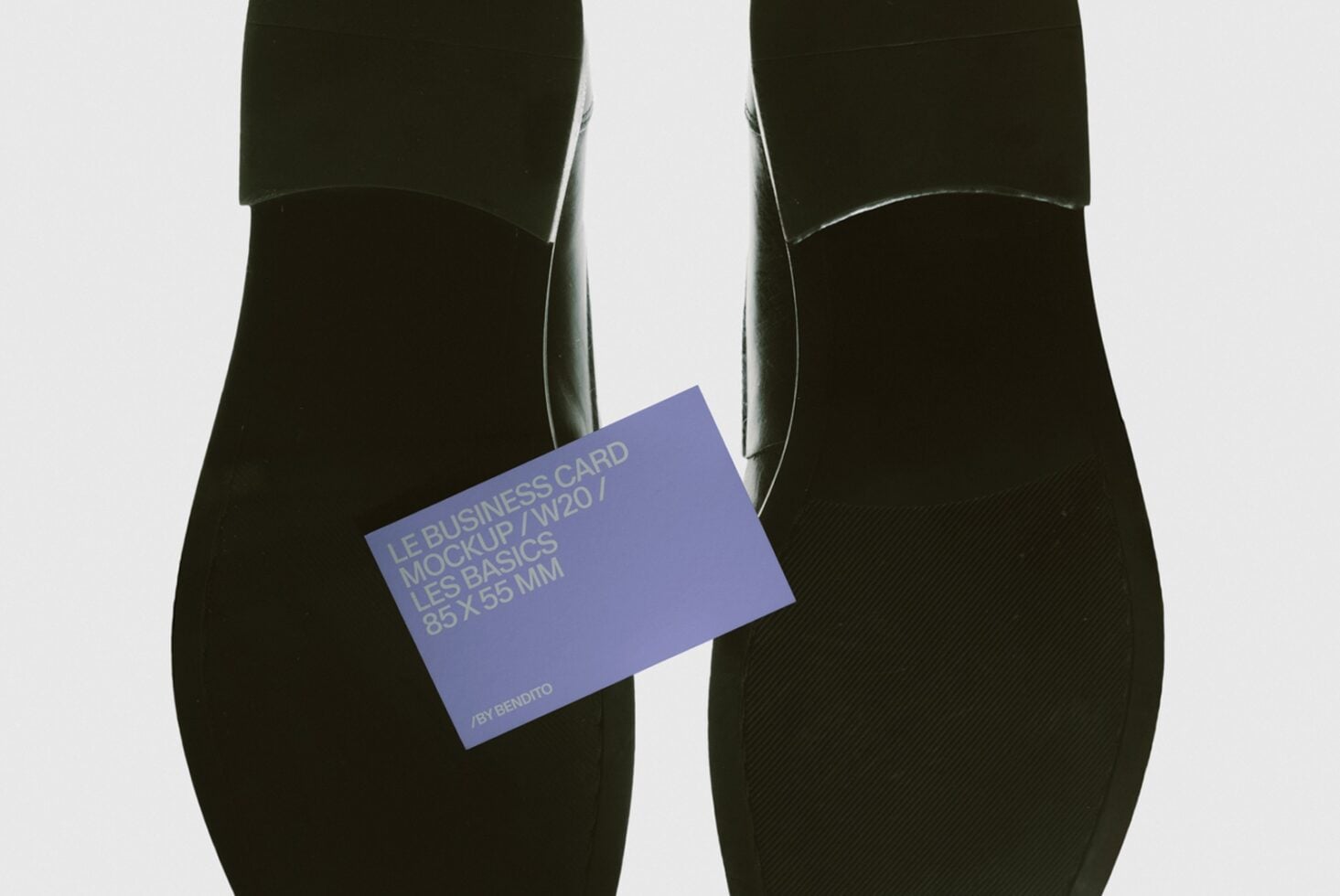 Periwinkle business card mockup held between black shoes, angled view
