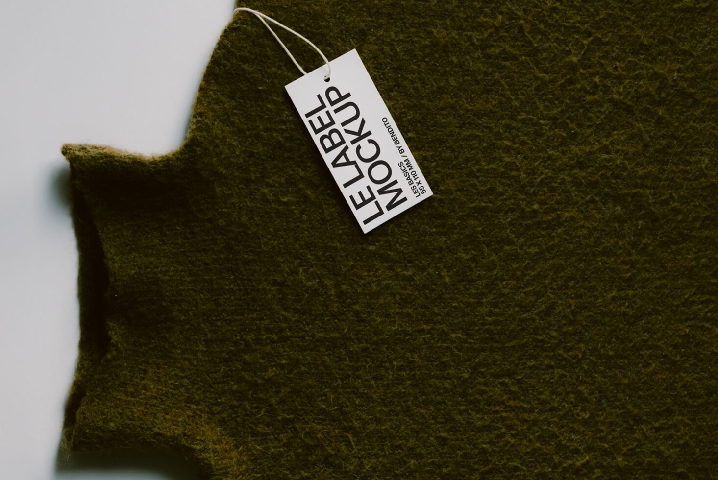 Olive wool sweater with white hang tag showing brand name, shot flat lay style on light background
