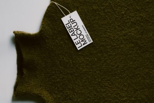 Olive wool sweater with white hang tag showing brand name, shot flat lay style on light background