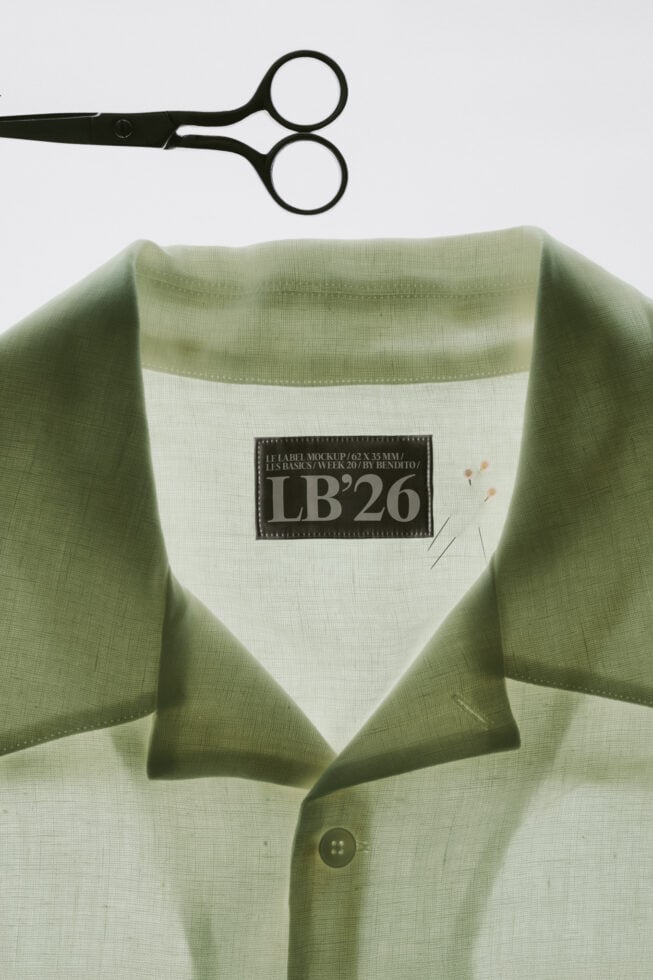 Black scissors above sage green shirt with woven label mockup on cream collar tag