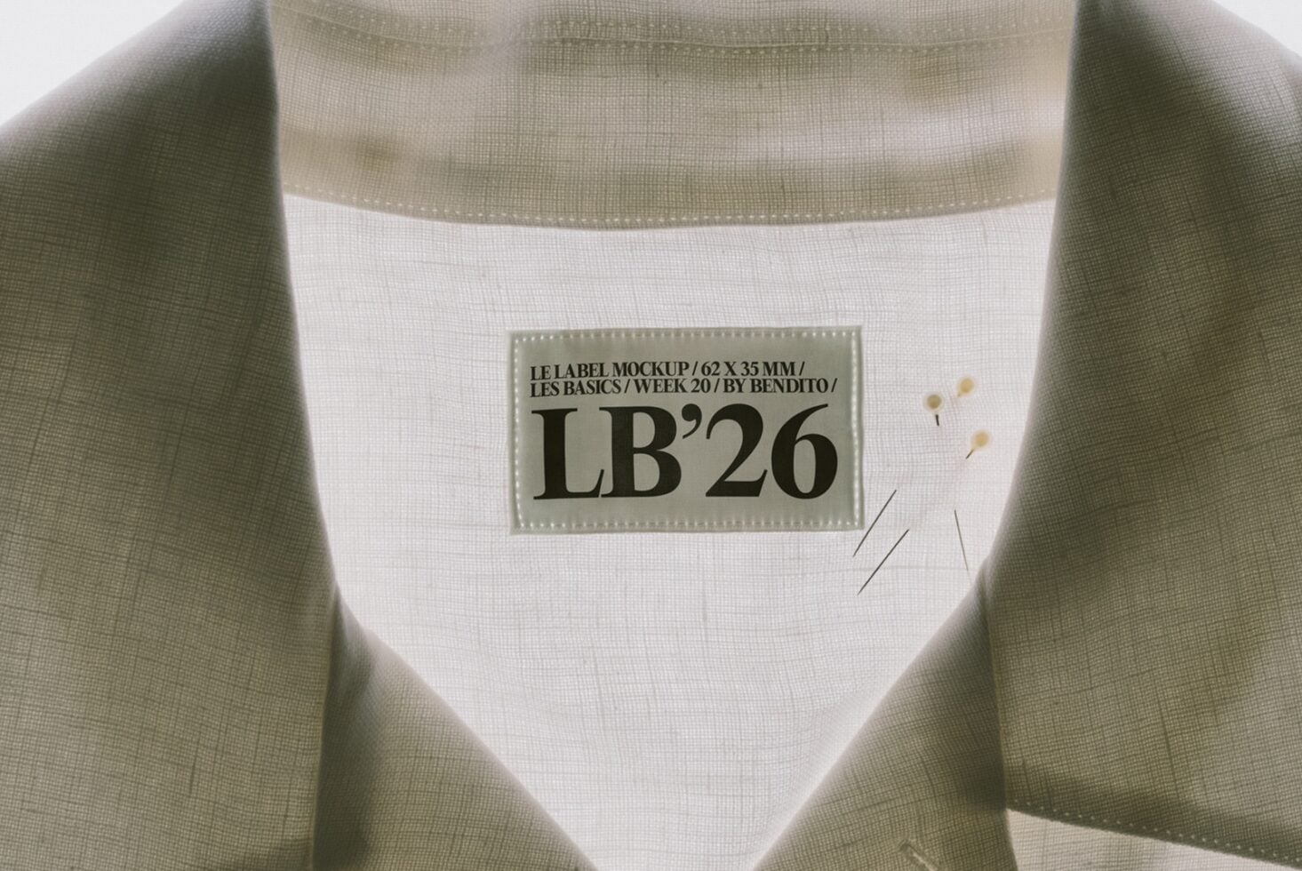 Clothing label mockup on sage ribbed fabric with stitched edges, showing 62x35mm tag design