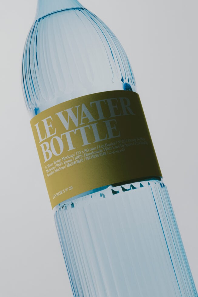 Clear water bottle with ribbed texture, olive label wrapping middle, multilingual text visible, minimal clean aesthetic