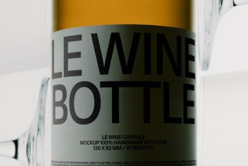 Wine bottle label mockup with gold bottle, gray wraparound label, black typography, next to glass