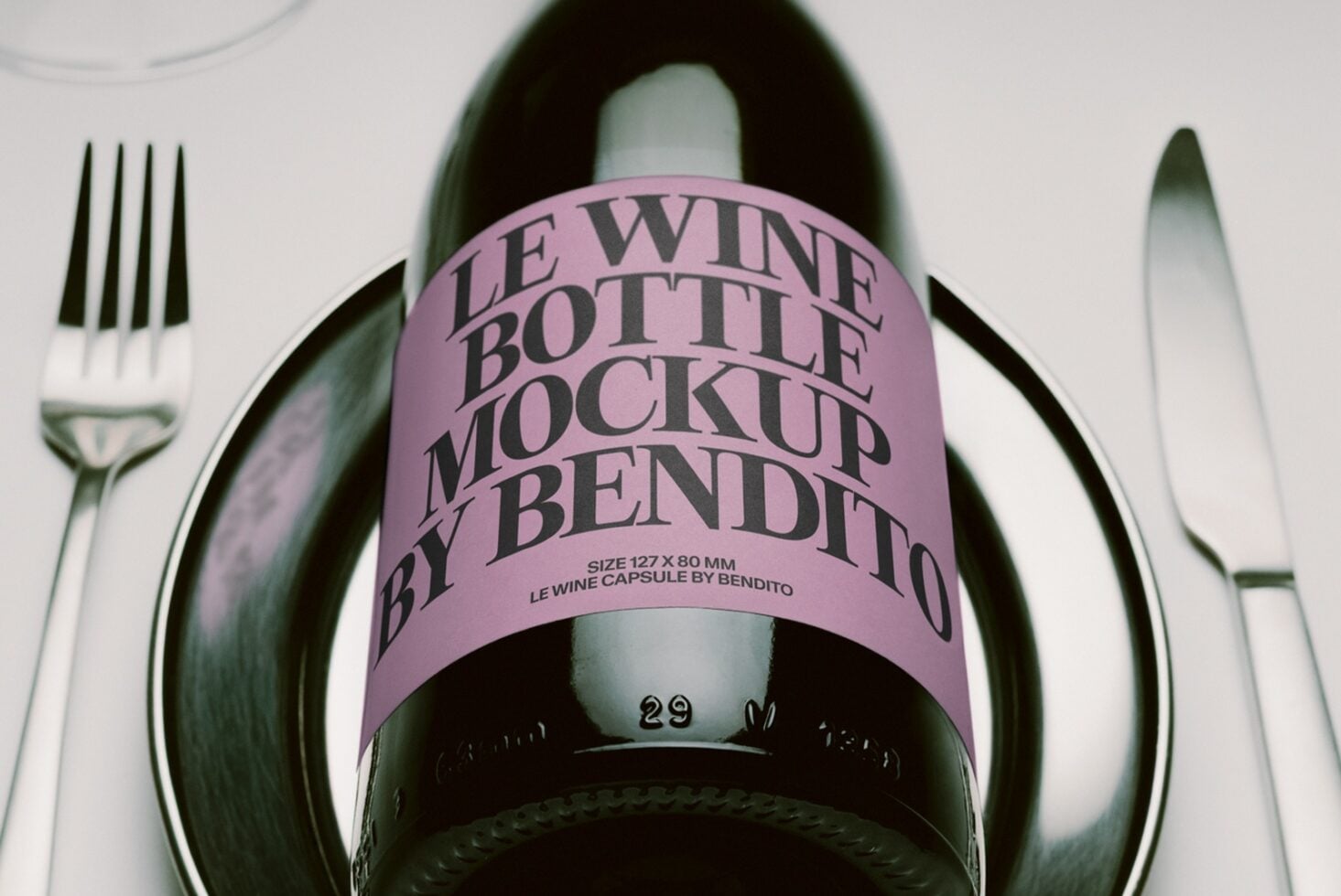Wine bottle with pink label sitting between fork plus knife on white surface