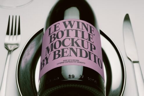 Wine bottle with pink label sitting between fork plus knife on white surface