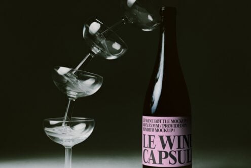 Wine bottle with pink label next to pouring glass with ice on dark background