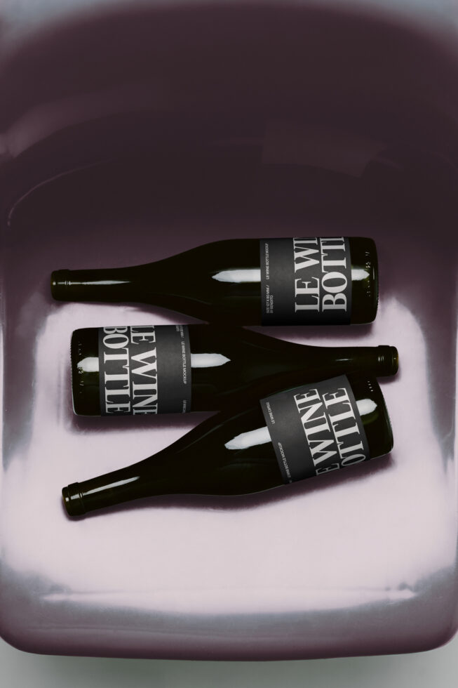 Three dark beer bottles with black labels arranged on a pink gradient background