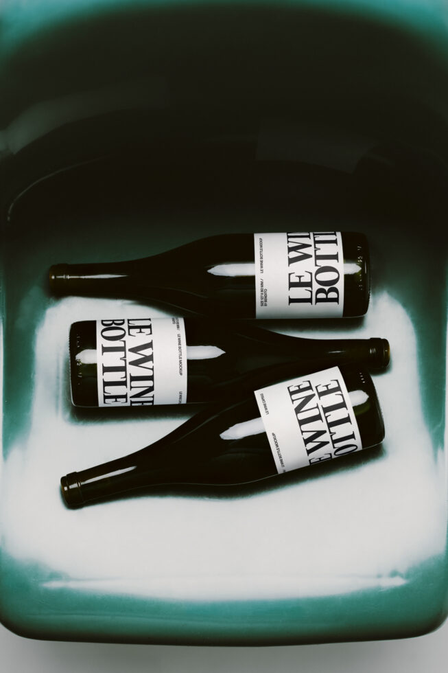 Three dark beer bottles with bold white labels on a soft teal surface with moody lighting