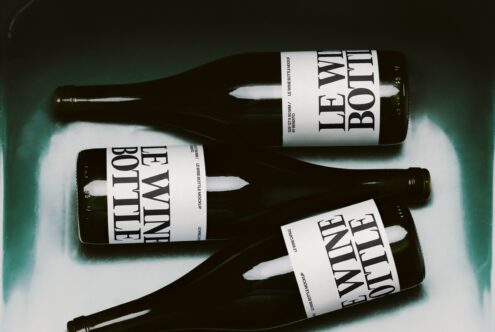 Dark wine bottles with bold serif labels on teal background, shot from above