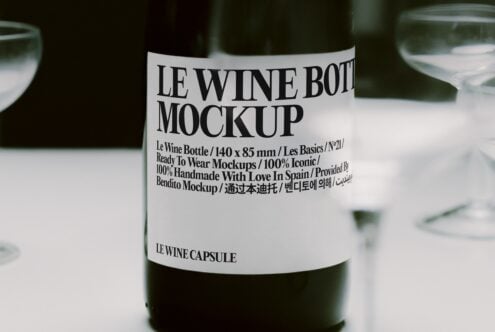 Close-up of wine bottle with minimalist label on white table, glasses blurred in background