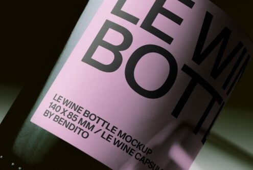 Wine bottle label mockup with pink surface, bold black typography, realistic product shot angled on dark background