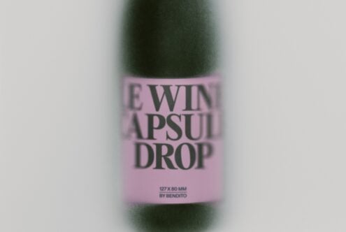 Blurred wine bottle with pink label showing "LEWIN APSULI DROP" text by Bendito