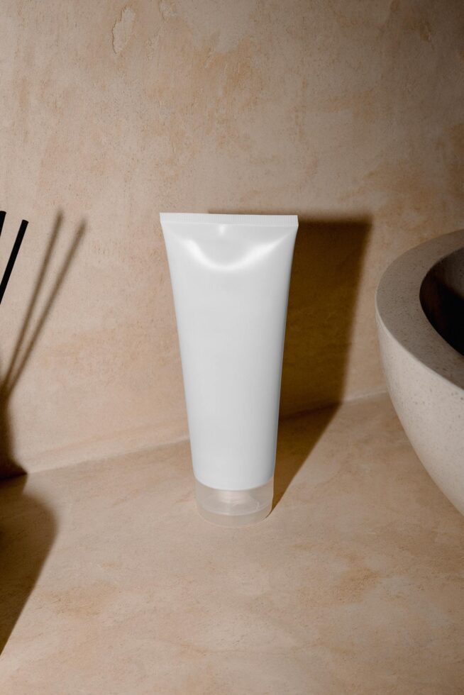 Blank white cosmetic tube mockup on beige textured background with natural shadows