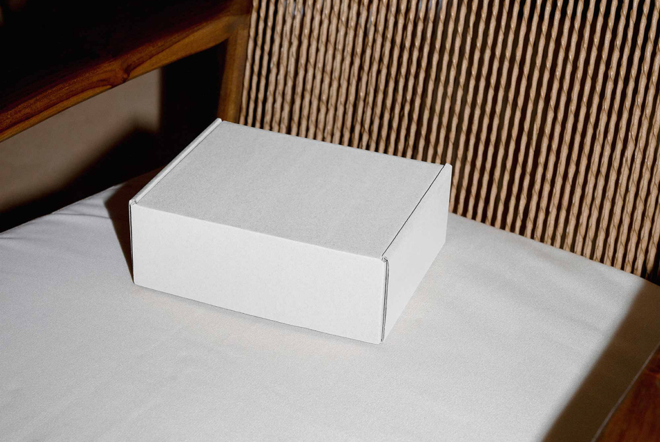 White cardboard box mockup on minimal desk with wood furniture in background
