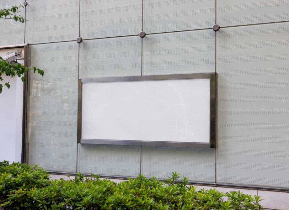 Blank storefront window display mounted on perforated metal wall with plants below