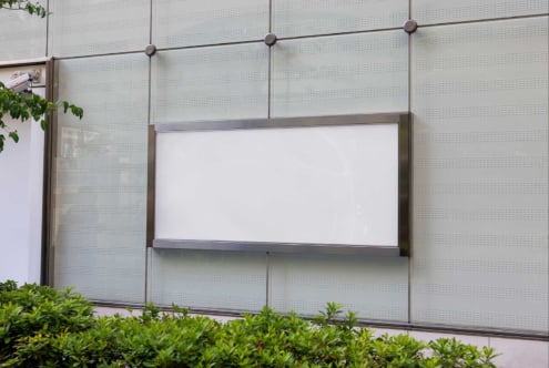 Blank storefront window mockup with perforated metal panels, greenery visible at bottom