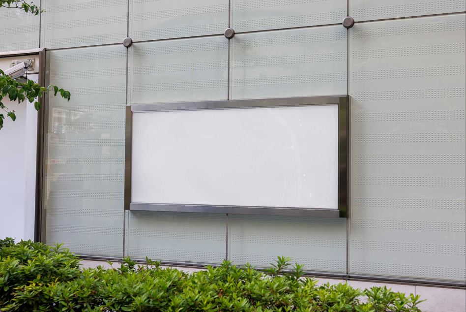 Blank storefront window mockup with perforated metal panels, greenery visible at bottom