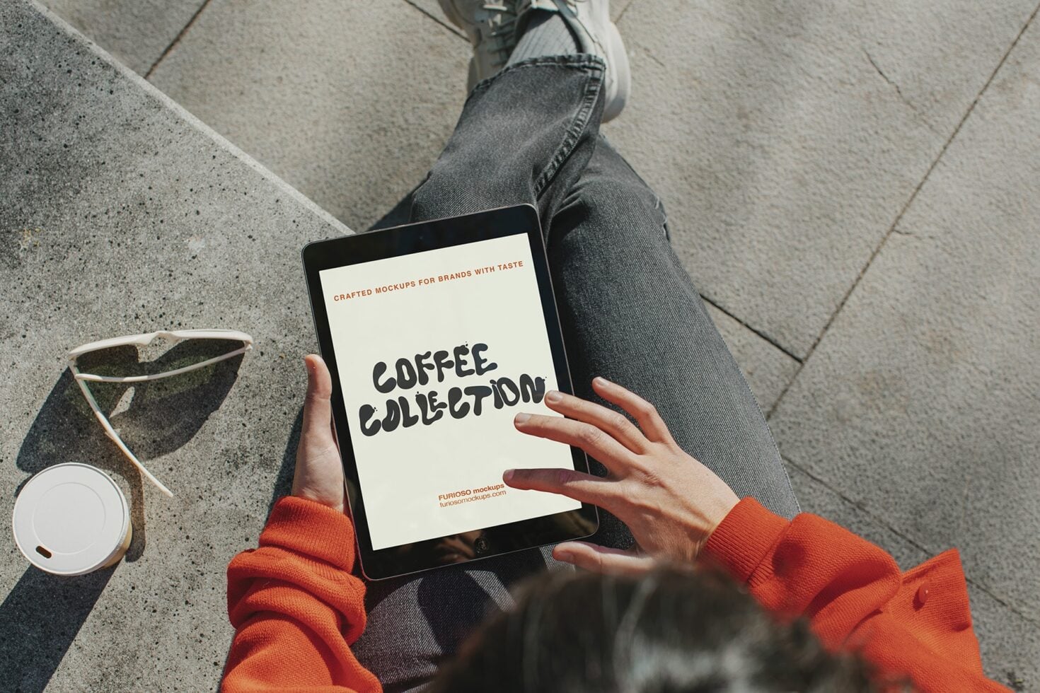 Overhead shot of person in orange sweater holding iPad displaying Coffee Collection branding mockup