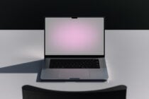 Open silver laptop with pink gradient screen displayed on white surface with dark backdrop