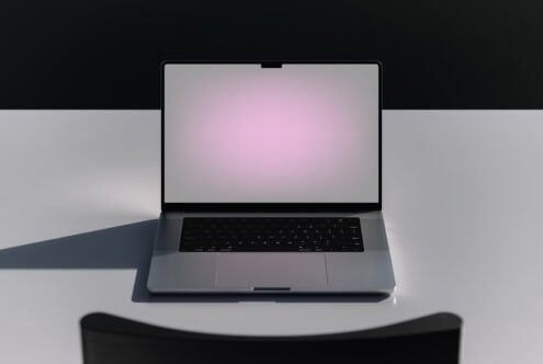 Open silver laptop with pink gradient screen displayed on white surface with dark backdrop