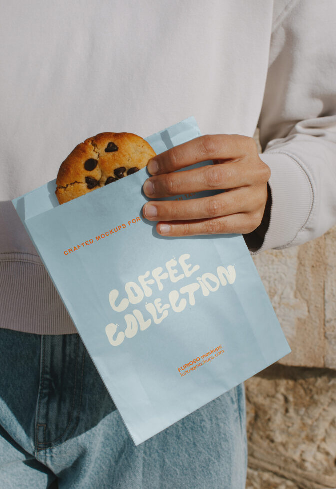 Close up of hands holding light blue paper with chocolate chip cookie sticking out