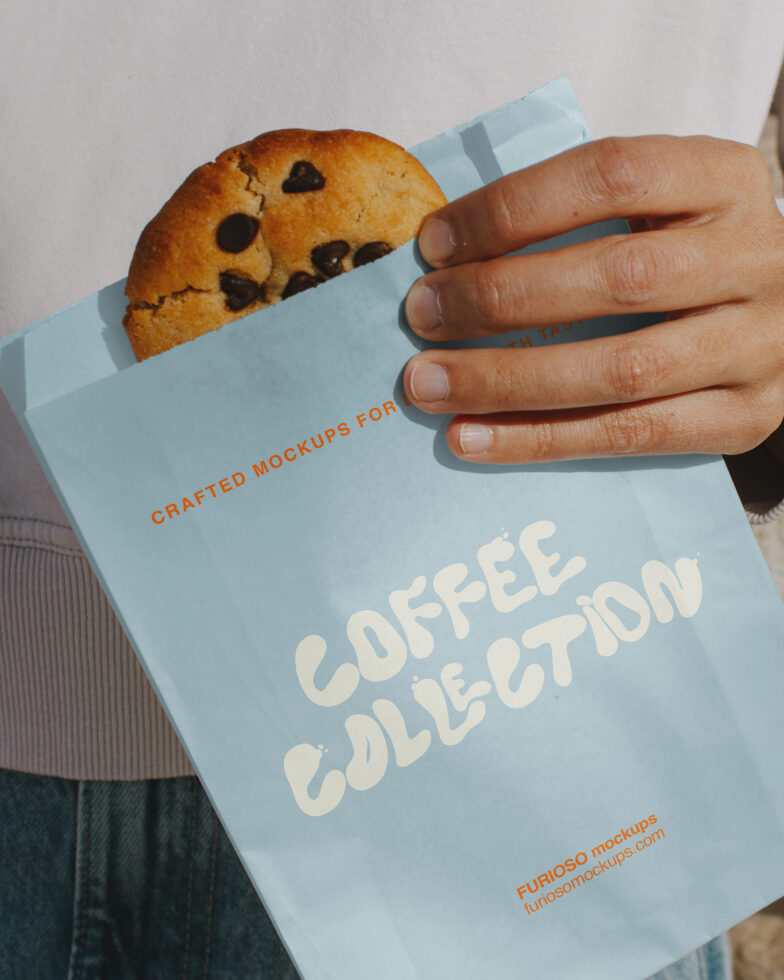 Hand holding light blue paper with chocolate chip cookie peeking out from top